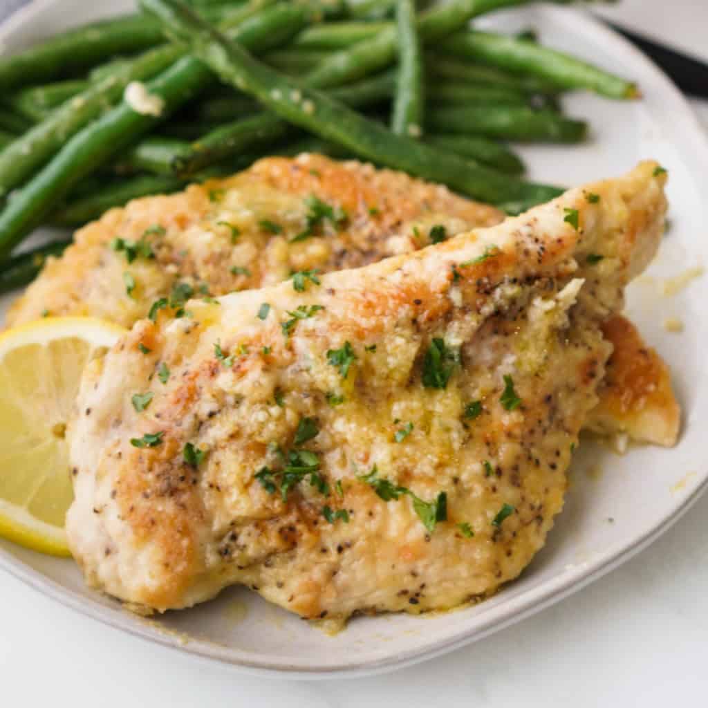 Two pieces of breaded chicken in lemon butter sauce on a plate with green beans