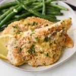 Two pieces of breaded chicken in lemon butter sauce on a plate with green beans