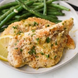 Two pieces of breaded chicken in lemon butter sauce on a plate with green beans