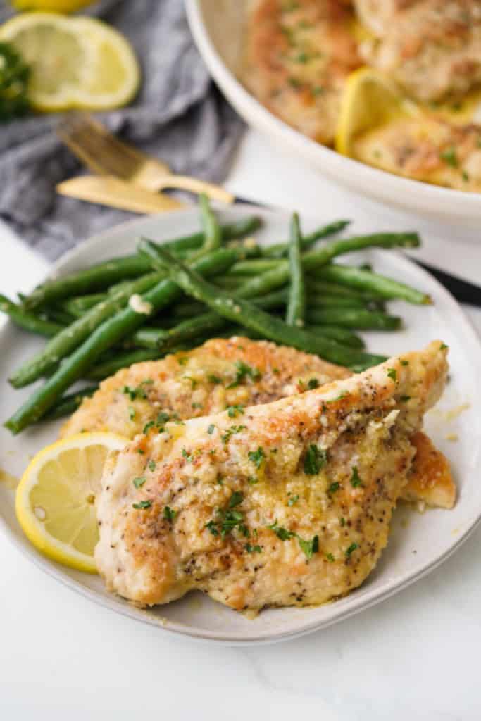 A plate has green beans and Lemon Butter chicken breasts with a lemon slice garnish.