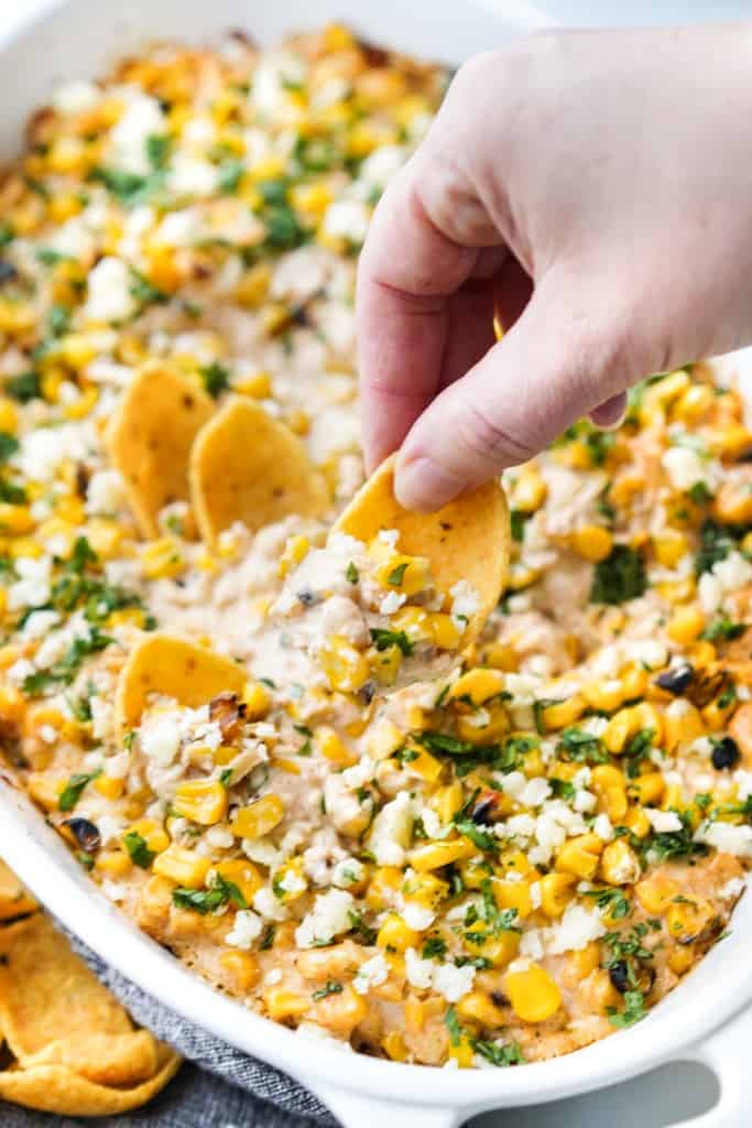 A corn chip is scooping up a bite of Mexican street corn dip.