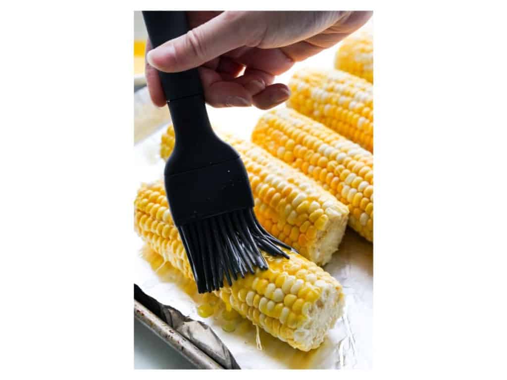 brushing melted butter on corn on the cob before baking