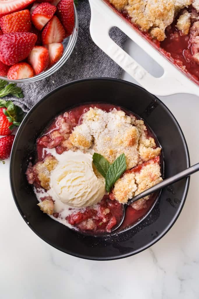A top-down picture of a gooey portion of fresh strawberry cobbler with vanilla ice cream.