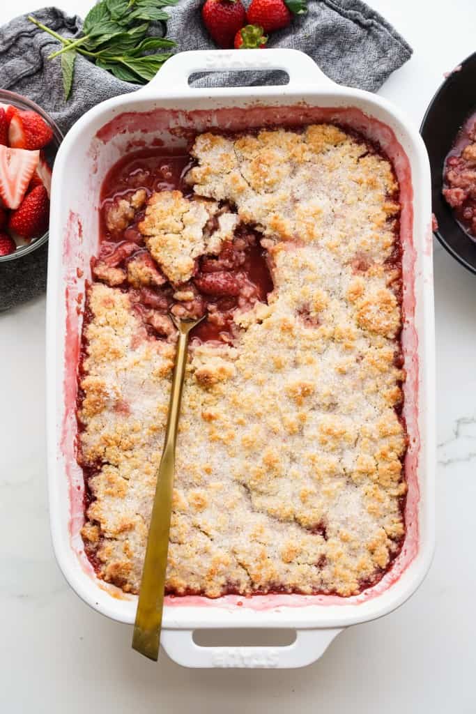 A spoon is scooping out a portion of Strawberry cobbler out of a rectangular baking dish.