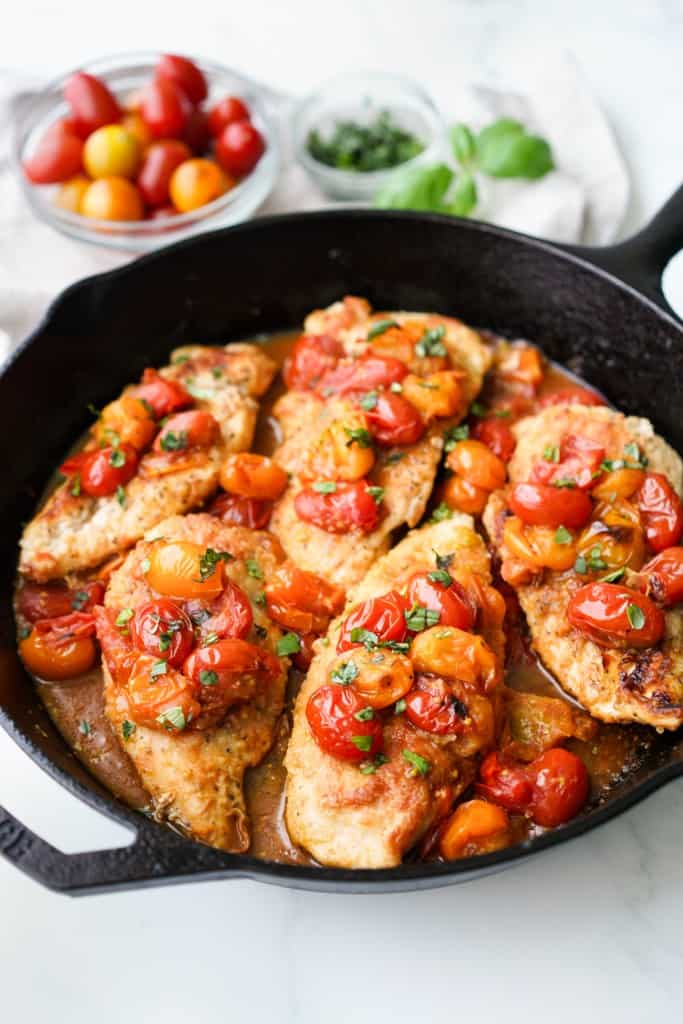 Chicken and tomatoes are in a cast iron skillet.