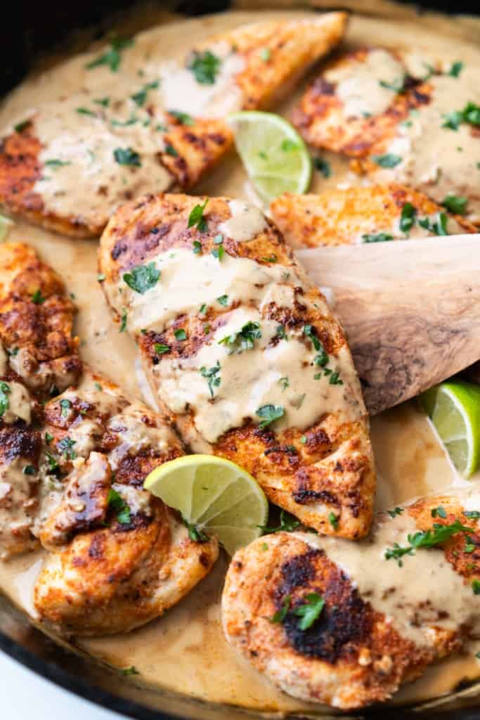 A spatula is lifting a creamy coconut lime chicken from a skillet.