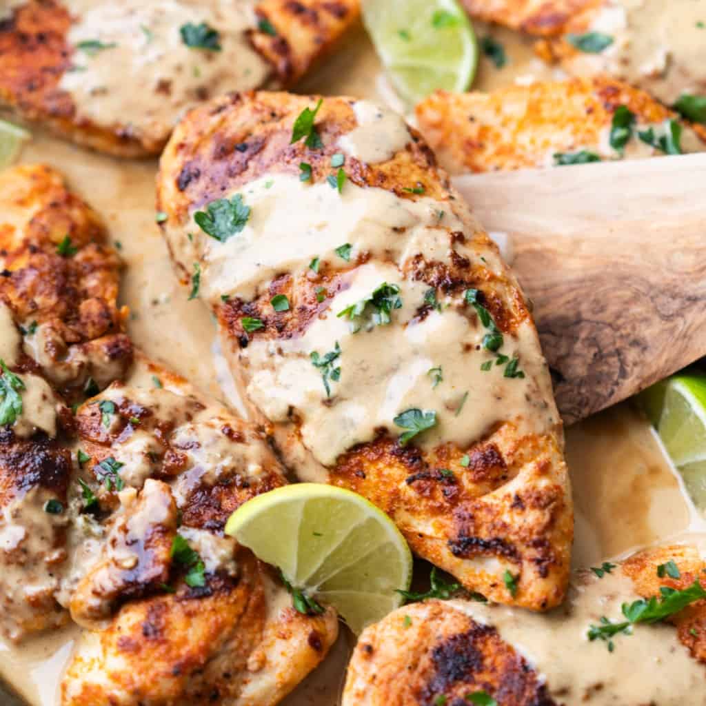 Close up picture of skillet coconut chicken garnished with lime wedges and parsley.