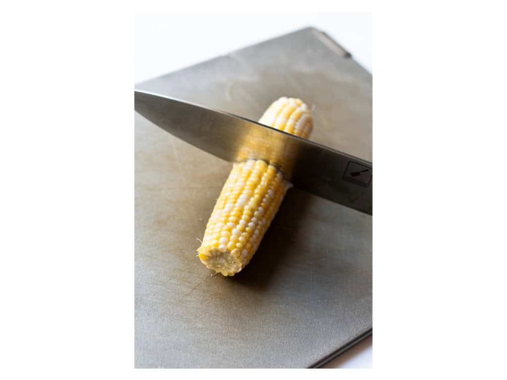 Fresh corn on the cob is cut in half length wise using a sharp knife.