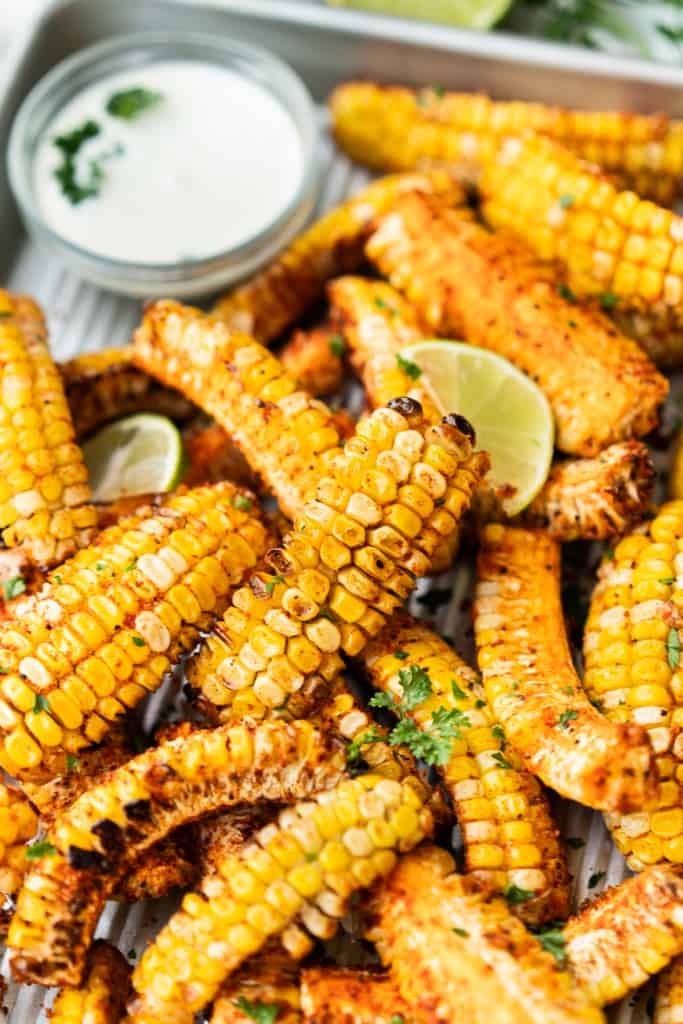 Corn ribs are piled high on a metal tray along side a dipping sauce.