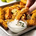 A hand is dipping a corn rib into ranch dressing.