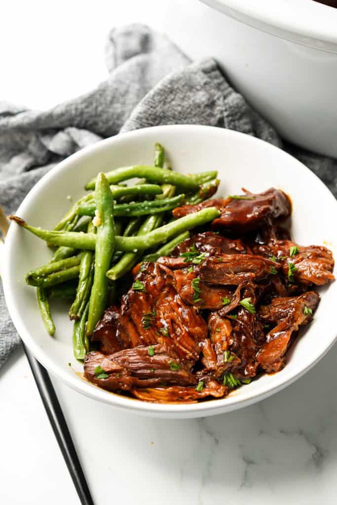 A plate of saucy shredded bbq beef with green beans
