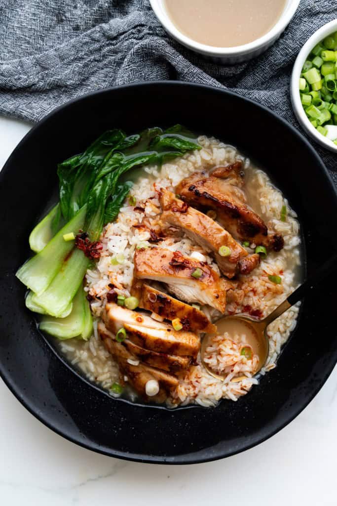 A spoon is resting in a bowl of brothy chicken and rice with bok choy.