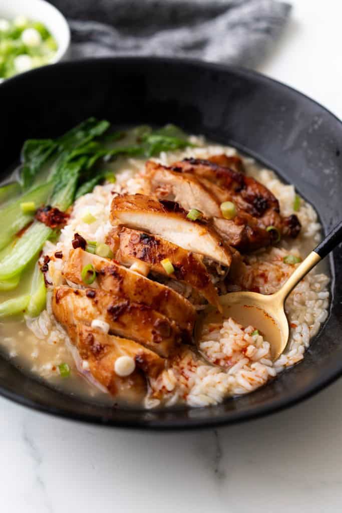 A spoon is scooping up brothy rice with chicken.