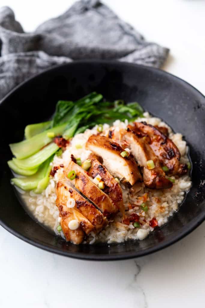 Brothy rice with marinated chicken is placed in a bowl with bok choy and topped with chili crisp.