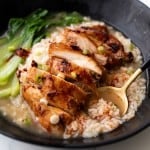 Delicious sliced chicken thigh is on top of a bowl of rice submerged in clear chicken broth