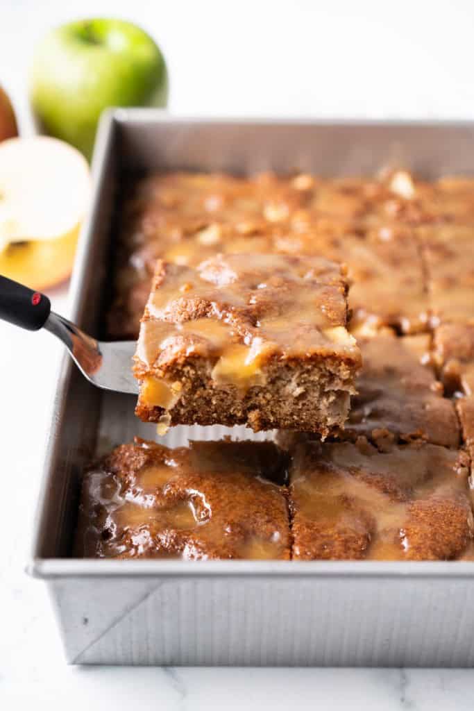 A slice of caramel apple cake is being lifted from a pan.
