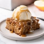 Caramel sauce is dripping down a scoop of ice cream sitting on top of a slice of caramel apple cake.