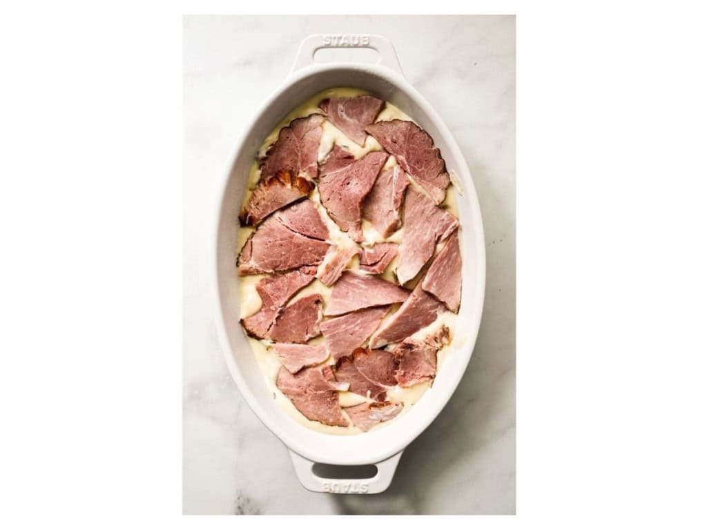 pieces of ham added to a casserole dish with potatoes and creamy cheese sauce