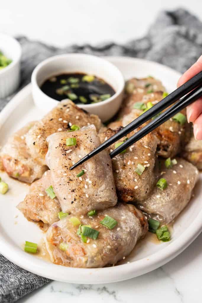A pair of chopsticks is lifting up a crispy rice paper dumpling from a plate.