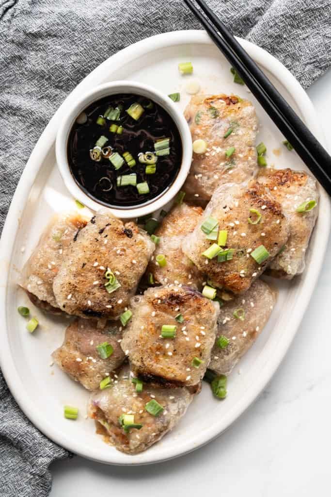 A pair of chopsticks is resting on a plate that is piled with rice paper dumplings filled with ground pork filling.