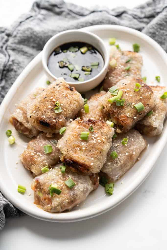 Rice paper wraps stuffed with ground pork and vegetable are piled on a plate and garnished with sesame seeds and green onions.