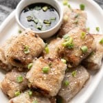 Fried rice paper rolls are stacked on a plate with a dumpling dipping sauce.