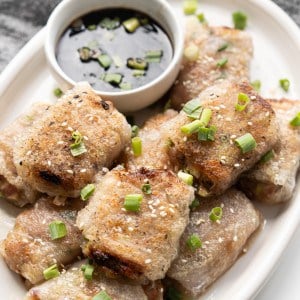 Fried rice paper rolls are stacked on a plate with a dumpling dipping sauce.