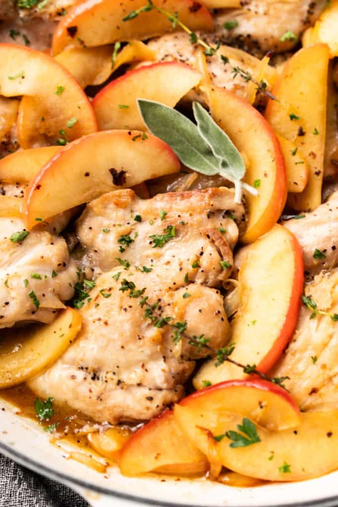 Fresh herbs sit on top of skillet apple cider glazed chicken.