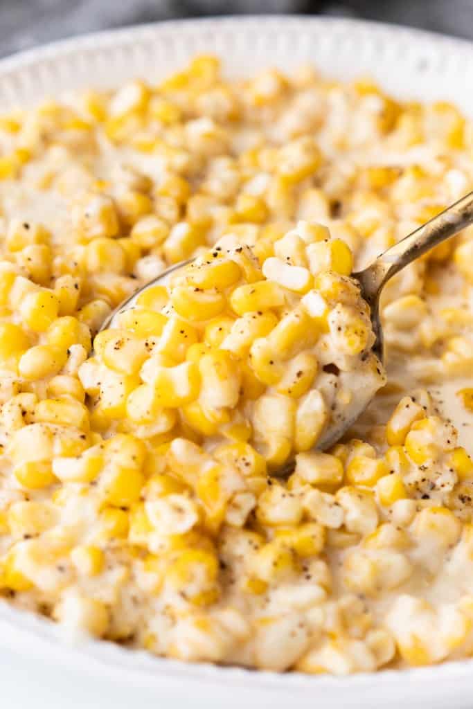Sweet creamy crockpot corn is being scooped with with a gold spoon.