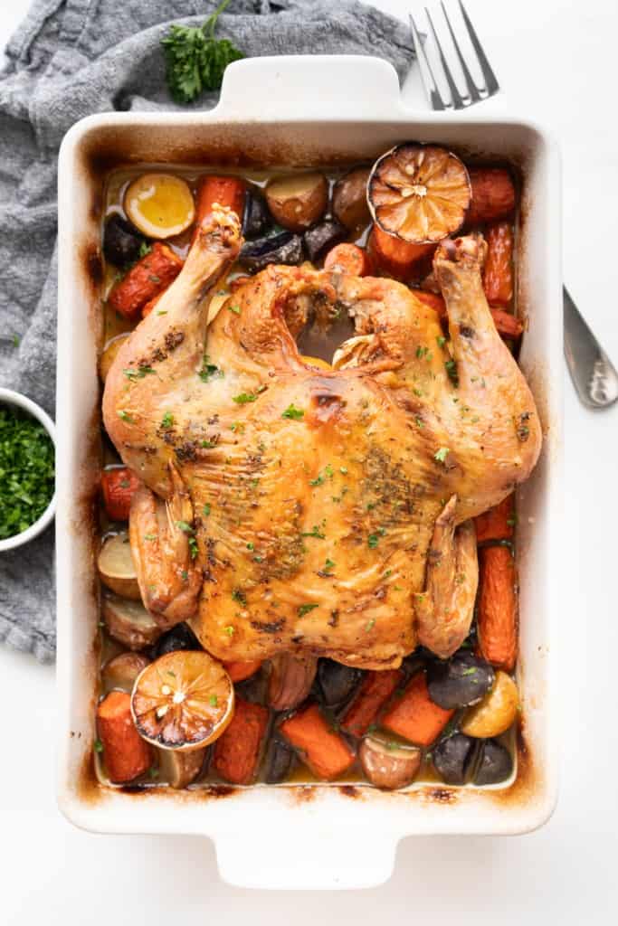 A baking dish is filled with a whole roasted chicken and veggies.