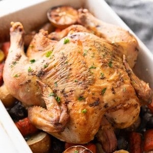Roasted whole chicken and vegetables are cooked and ready to be carved.