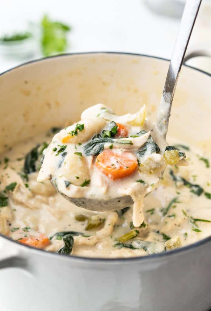 A ladle is overflowing with Creamy Chicken Gnocchi Soup.